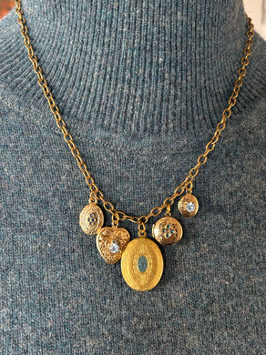 Gold locket charm necklace on a gray sweater