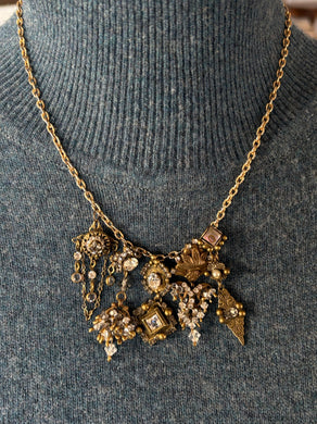 Gold victorian charm necklace with intricate designs and pendants on a gray sweater.