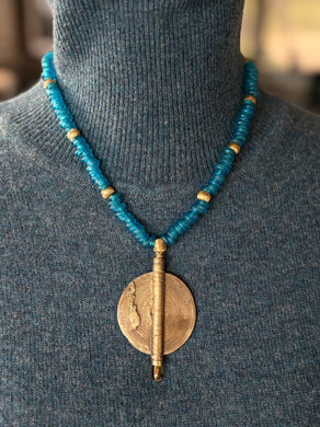 Necklace with blue recycled glass beads and a brass African pendant on a gray sweater.