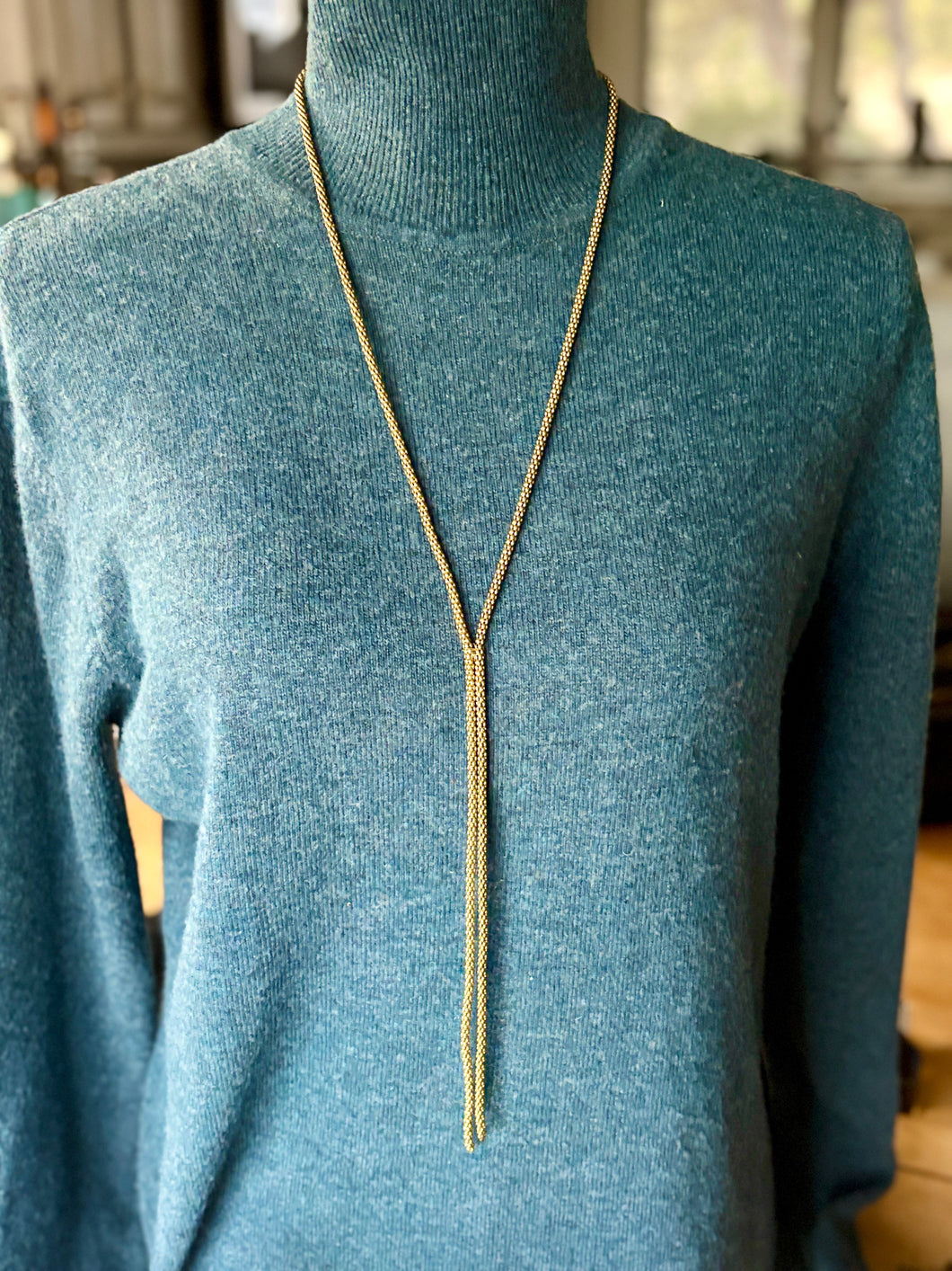 Brass bolo necklace on a mannequin wearing a teal sweater