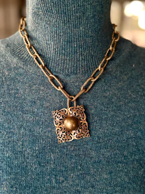 Bronze paperclip chain necklace with a decorative pendant on a mannequin wearing a blue sweater.