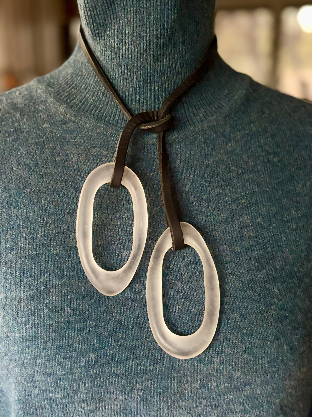 Necklace with large lucite oval pendants on a mannequin wearing a blue sweater.